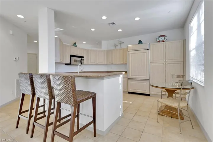 Kitchen featuring a kitchen bar, light tile patterned flooring, recessed lighting, paneled fridge, and stainless steel microwave