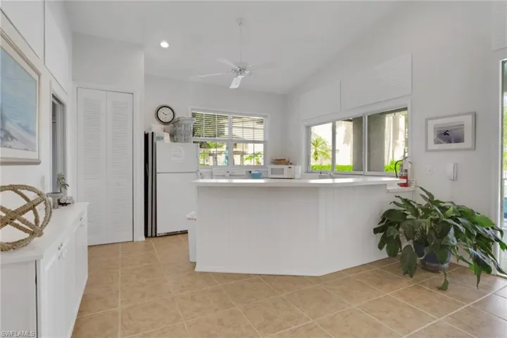 Kitchen with light countertops, white appliances, light tile patterned floors, ceiling fan, and white cabinets