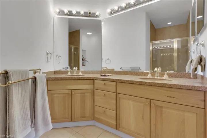 Full bathroom with double vanity, light tile patterned floors, and a shower stall