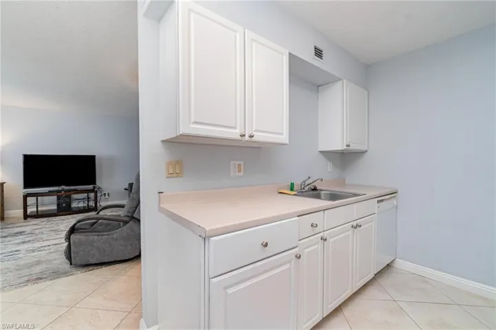 Kitchen with light countertops, light tile patterned flooring, white cabinets, open floor plan, and white dishwasher