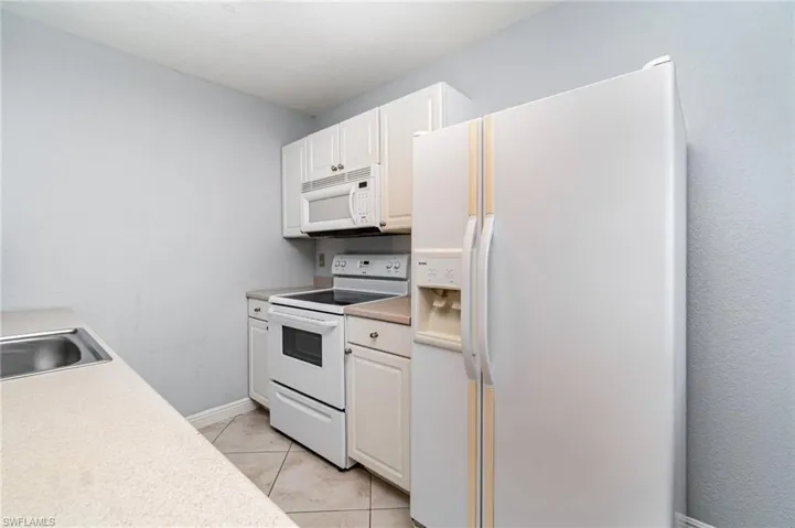 Kitchen with white appliances, white cabinets, light countertops, and light tile patterned floors