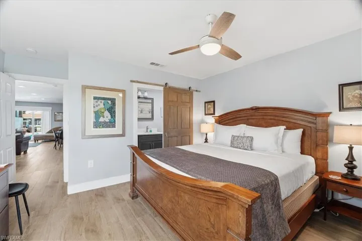 Bedroom with a barn door, connected bathroom, wood finished floors, and a ceiling fan