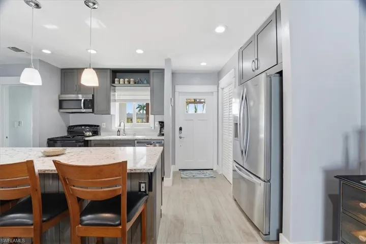 Kitchen featuring gray cabinets, appliances with stainless steel finishes, decorative light fixtures, light stone counters, and recessed lighting