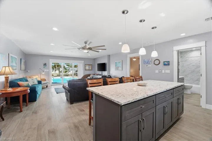 Kitchen with a kitchen breakfast bar, a center island, light stone countertops, hanging light fixtures, and ceiling fan