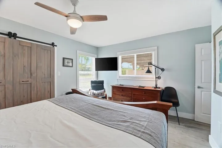 Bedroom featuring a barn door, light wood-type flooring, ceiling fan, and a closet