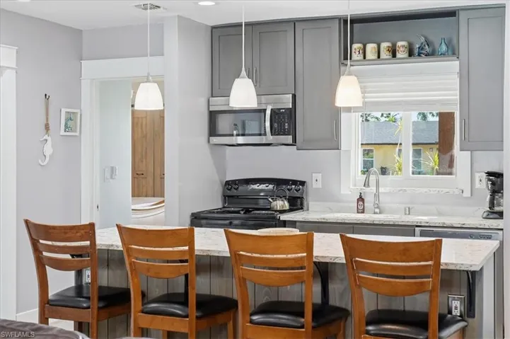 Kitchen featuring stainless steel appliances, a breakfast bar area, pendant lighting, and light stone countertops