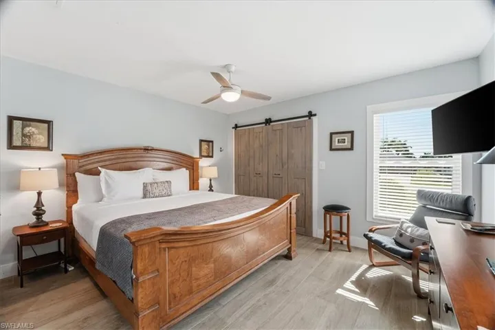 Bedroom featuring a barn door, ceiling fan, light wood finished floors, and an office area