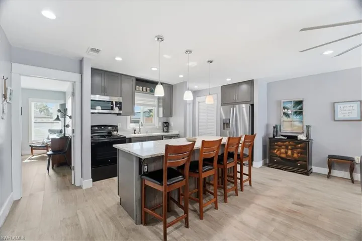 Kitchen with a kitchen breakfast bar, gray cabinets, appliances with stainless steel finishes, a center island, and hanging light fixtures