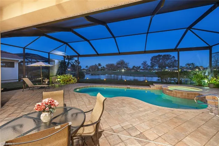 View of swimming pool featuring a patio area, an in ground hot tub, a water view, and glass enclosure