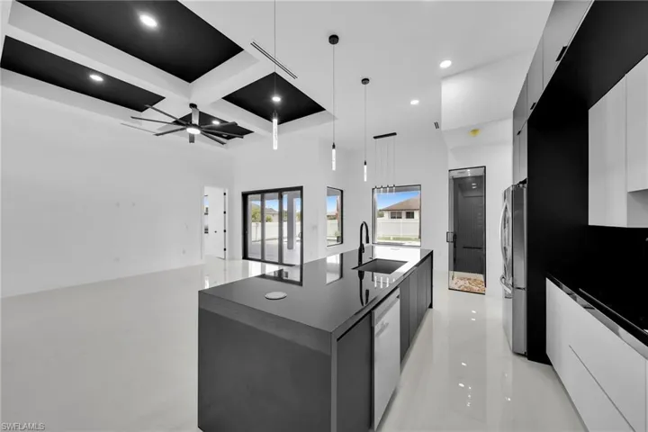 Kitchen with a kitchen island with sink, ceiling fan, appliances with stainless steel finishes, coffered ceiling, and pendant lighting