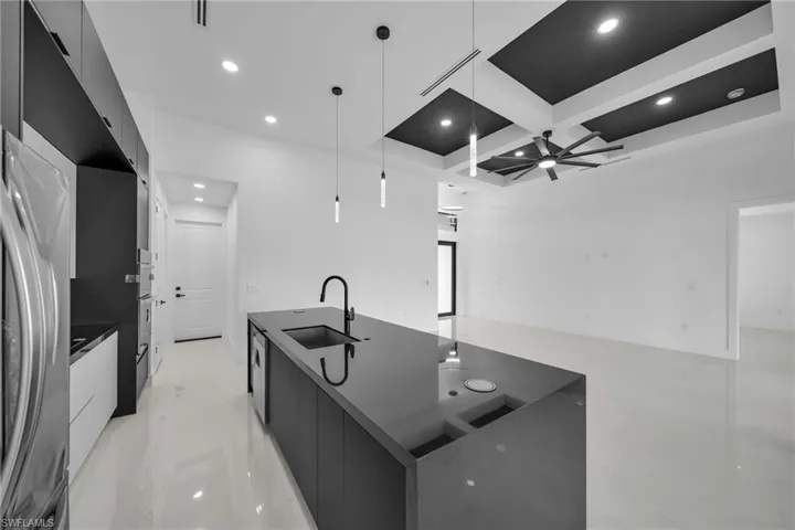 Kitchen with an island with sink, ceiling fan, hanging light fixtures, coffered ceiling, and sink