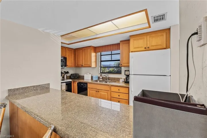 Kitchen featuring light stone countertops, sink, and black appliances