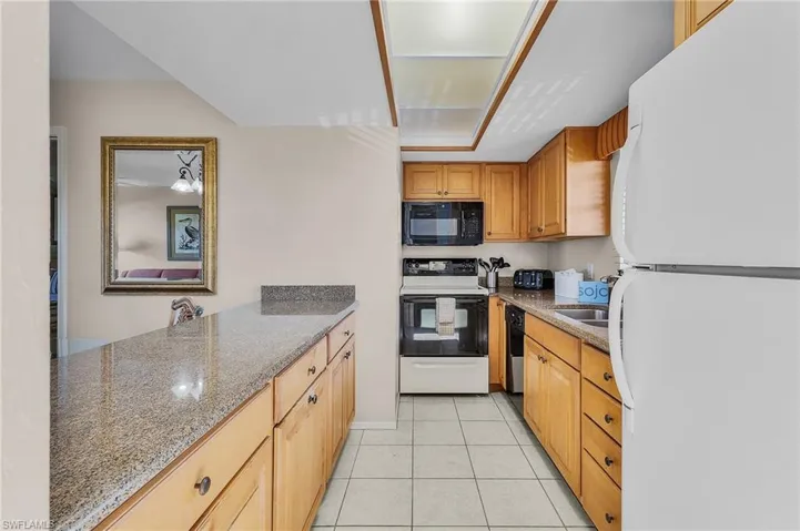 Kitchen with stone counters, sink, light tile patterned floors, and black appliances