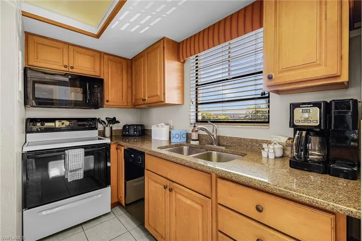 Kitchen with range with electric stovetop, light stone countertops, sink, and light tile patterned floors