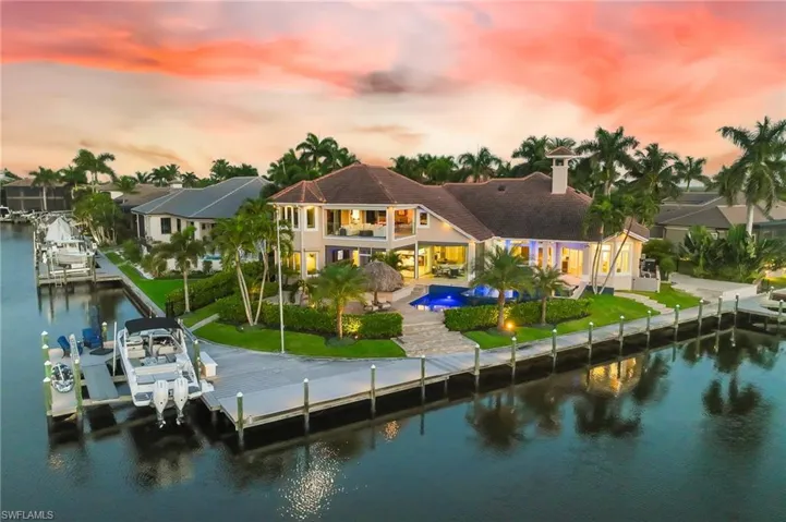 Back of property at dusk featuring an outdoor pool, a water view, boat lift, a patio area, and a balcony