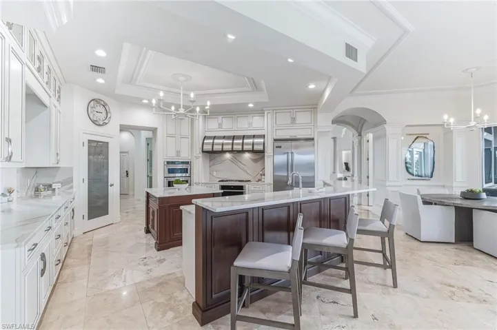 Kitchen with a chandelier, dark brown cabinets, light stone counters, pendant lighting, and glass insert cabinets