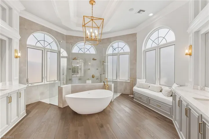 Bathroom featuring two vanities, walk in shower, crown molding, dark wood-style flooring, and a freestanding tub