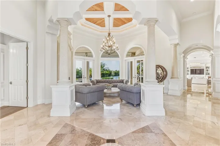 Living room featuring ornate columns, a high ceiling, a chandelier, french doors, and ornamental molding