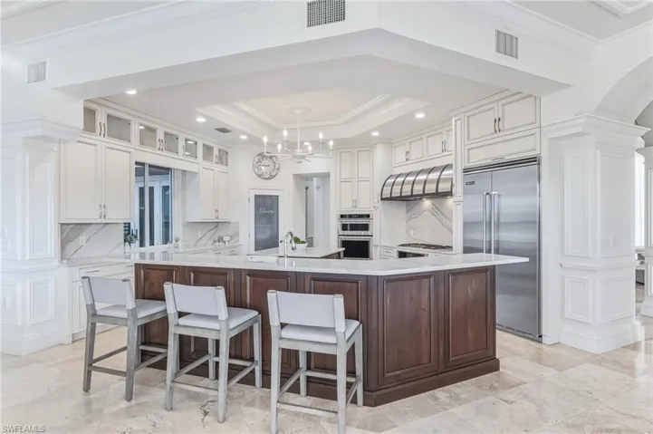 Kitchen featuring ornamental molding, appliances with stainless steel finishes, white cabinets, light stone counters, and ornate columns