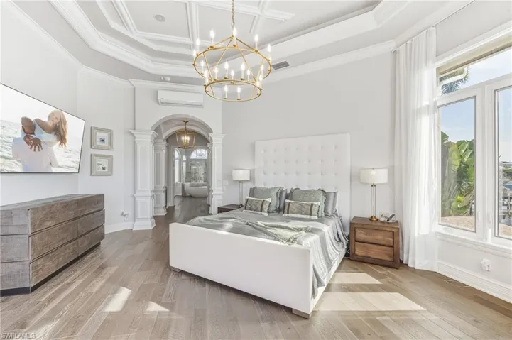 Bedroom with arched walkways, a high ceiling, light wood-style flooring, coffered ceiling, and a chandelier