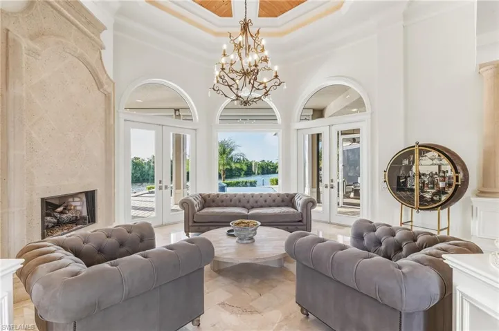Living area with french doors, a raised ceiling, crown molding, a chandelier, and a high ceiling