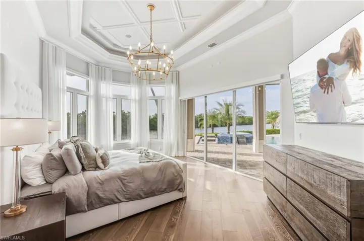 Bedroom with crown molding, wood-type flooring, coffered ceiling, access to outside, and a high ceiling