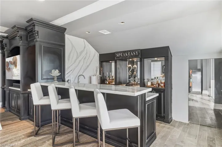 Kitchen with dark cabinets, a breakfast bar area, light stone countertops, light wood-style flooring, and recessed lighting