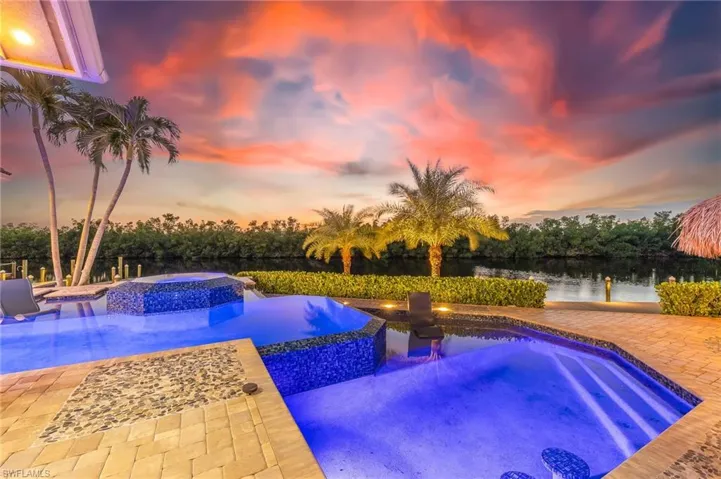 Pool at dusk featuring a pool with connected hot tub, a patio, and a water view