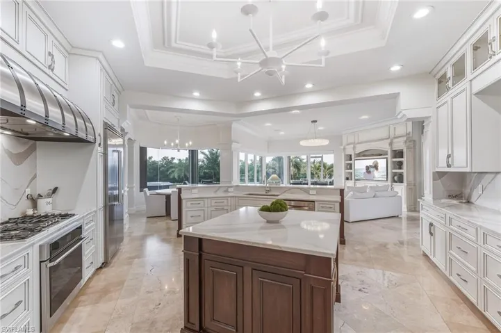 Kitchen with a tray ceiling, a chandelier, ornamental molding, open floor plan, and an island with sink