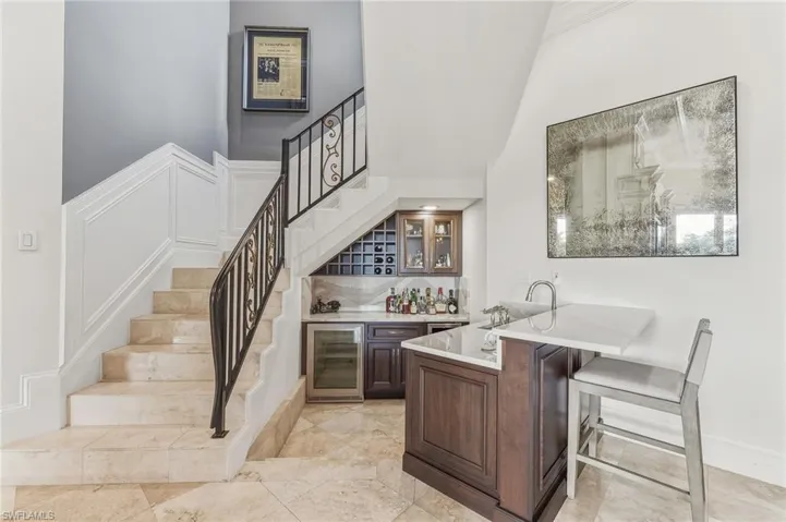 Indoor wet bar featuring glass insert cabinets, stairway, wine cooler, and light stone counters