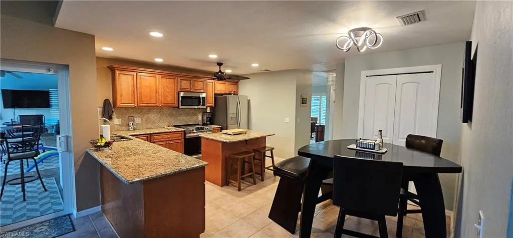 Kitchen with light stone counters, a kitchen island, appliances with stainless steel finishes, decorative backsplash, and a breakfast bar