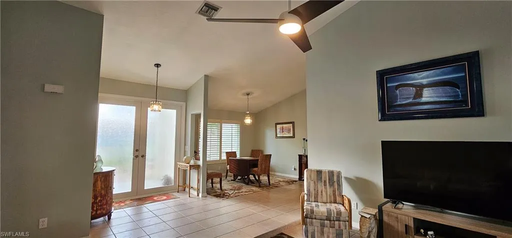 Tiled living room featuring vaulted ceiling, ceiling fan, and french doors