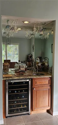 Bar featuring beverage cooler, sink, light tile patterned flooring, and stone countertops