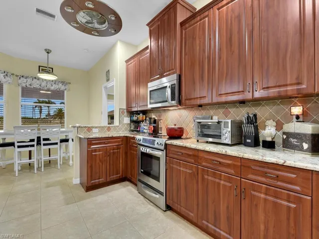 Kitchen featuring light stone counters, pendant lighting, light tile patterned flooring, backsplash, and stainless steel appliances