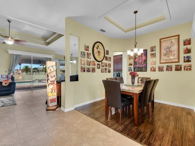 Dining space featuring ceiling fan with notable chandelier, light wood-type flooring, and a tray ceiling