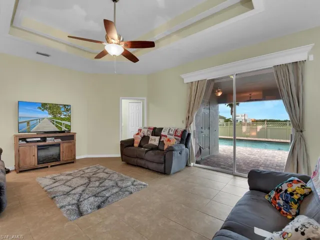 Living room with ceiling fan, light tile patterned flooring, and a raised ceiling