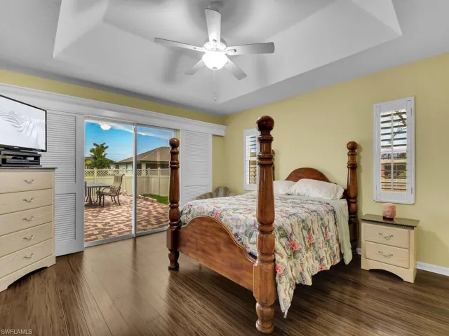 Bedroom featuring ceiling fan, a tray ceiling, dark wood-type flooring, and access to exterior