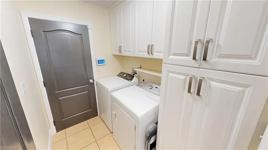 Laundry room featuring light tile patterned flooring, washing machine and dryer, and cabinets