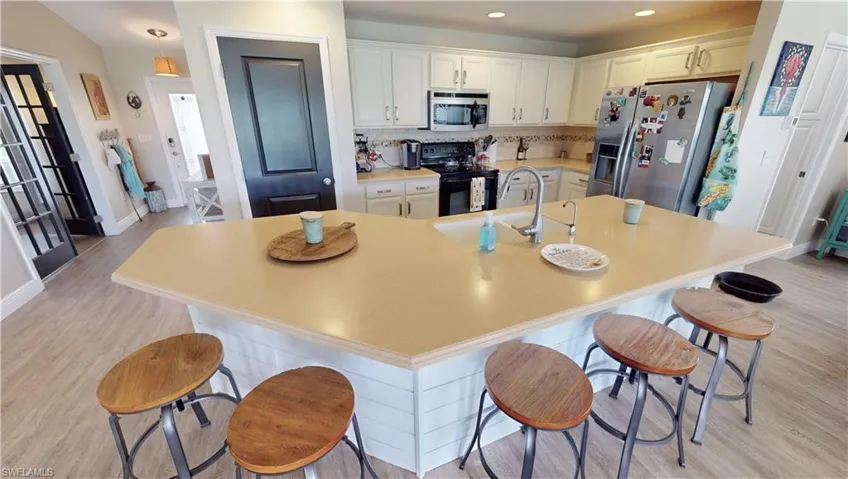 Kitchen featuring light hardwood / wood-style floors, appliances with stainless steel finishes, a kitchen bar, and a spacious island
