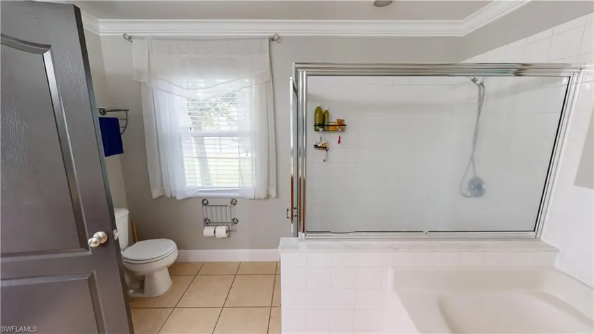 Bathroom with ornamental molding, toilet, tile patterned floors, and separate shower and tub