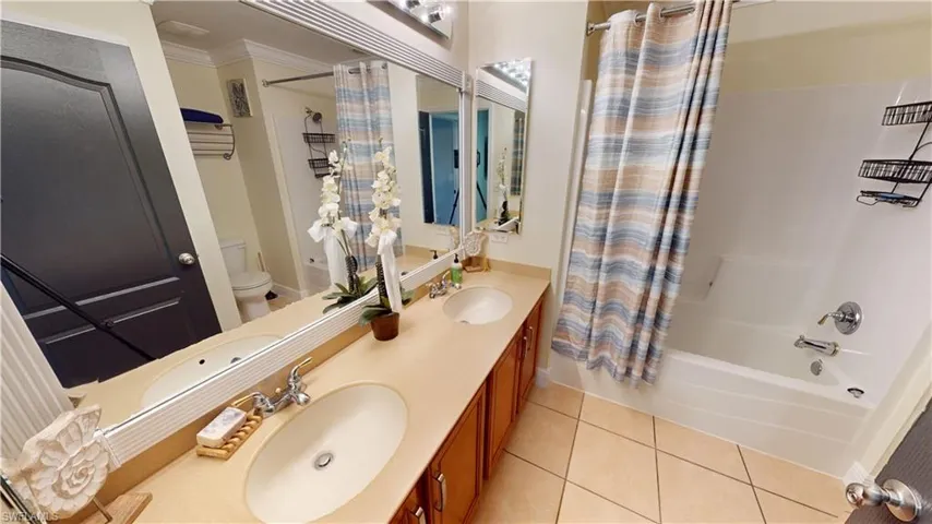 Full bathroom featuring tile patterned flooring, double vanity, toilet, shower / tub combo, and ornamental molding