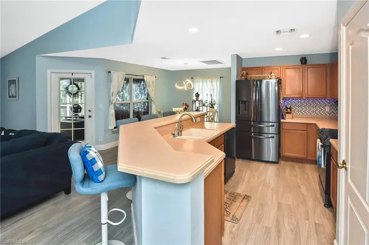 Kitchen featuring an island with sink, black electric range oven, light hardwood / wood-style floors, stainless steel fridge, and sink