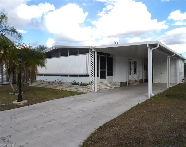 View of front of property with entry steps, driveway, a carport, and a front yard