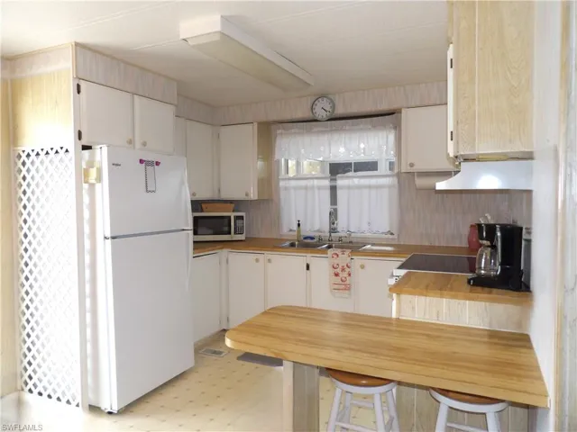 Kitchen featuring light flooring, freestanding refrigerator, butcher block counters, stainless steel microwave, and range hood