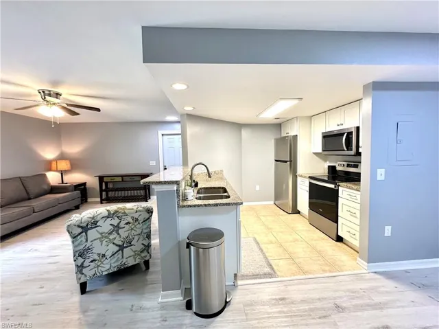 Kitchen with stainless steel appliances, kitchen peninsula, sink, ceiling fan, and light stone countertops
