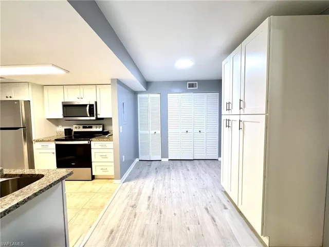 Kitchen with light hardwood / wood-style flooring, appliances with stainless steel finishes, light stone counters, white cabinetry, and sink