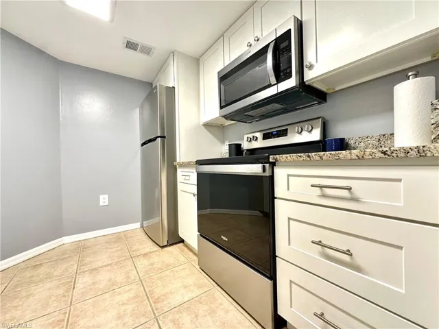 Kitchen featuring light tile patterned floors, appliances with stainless steel finishes, white cabinetry, and light stone countertops