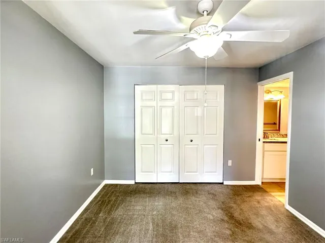 Unfurnished bedroom featuring connected bathroom, sink, ceiling fan, a closet, and carpet flooring