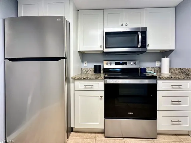 Kitchen with dark stone countertops, light tile patterned floors, appliances with stainless steel finishes, and white cabinetry