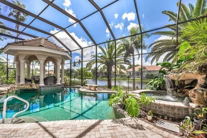 View of swimming pool with a patio area, a water view, pool water feature, glass enclosure, and a jacuzzi
